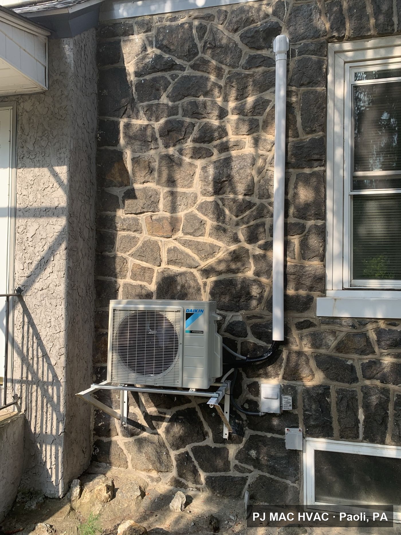 Daikin ductless mini-split condenser mounted on a stone home exterior