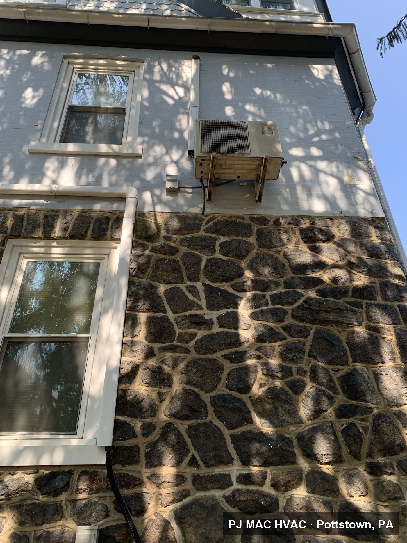 PJ MAC HVAC mini-split condenser installed on a wall bracket on the upper exterior of a stone Philadelphia-area house.