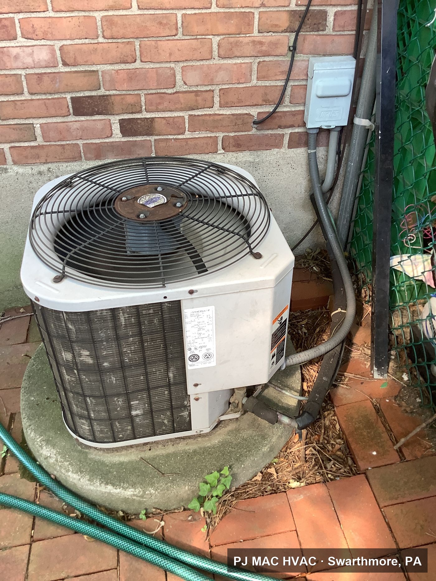 A residential AC condenser installed by PJ MAC HVAC on a pad beside a brick home.