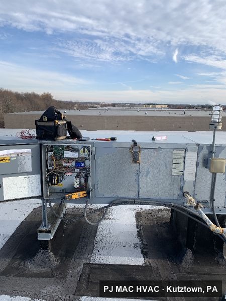A PJ MAC HVAC technician repairs the controls of a commercial rooftop unit.