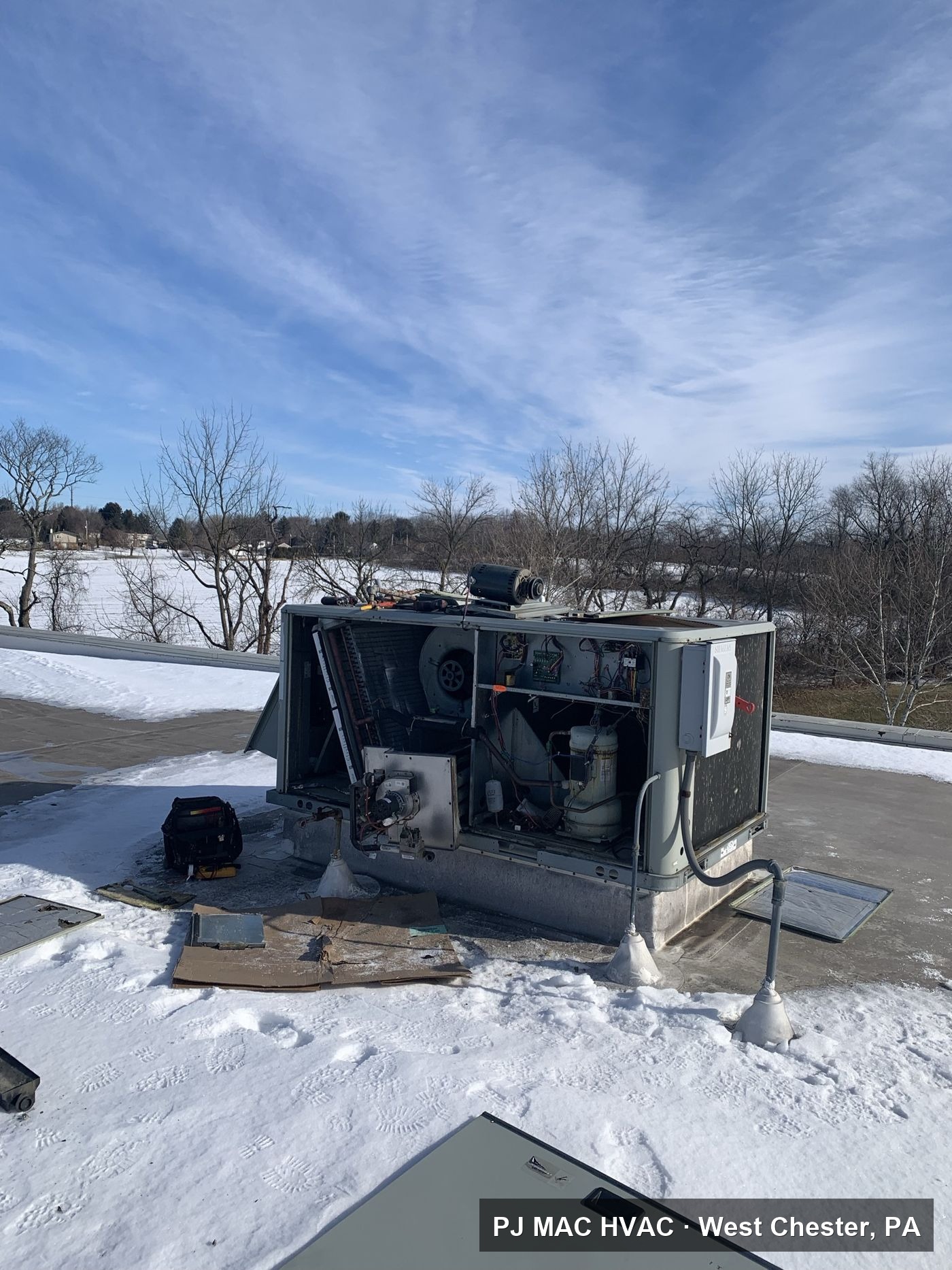 PJ MAC HVAC servicing an opened commercial rooftop unit on a snowy roof.