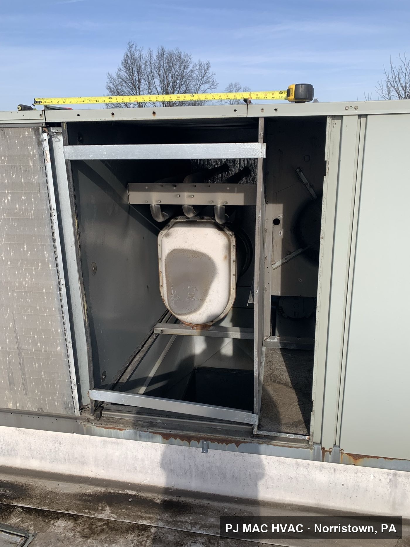 PJ MAC HVAC inspecting the heat exchanger inside an opened commercial rooftop unit.