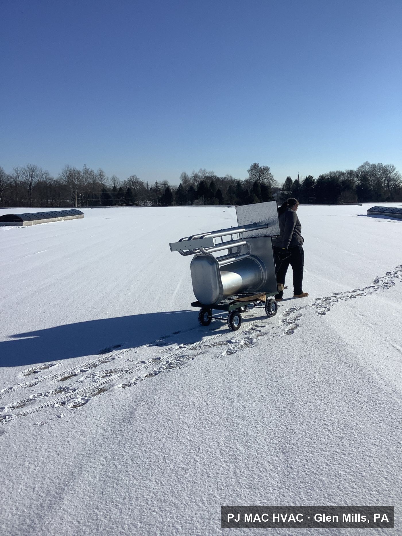 PJ MAC technician hauling parts across a snowy roof on an emergency call